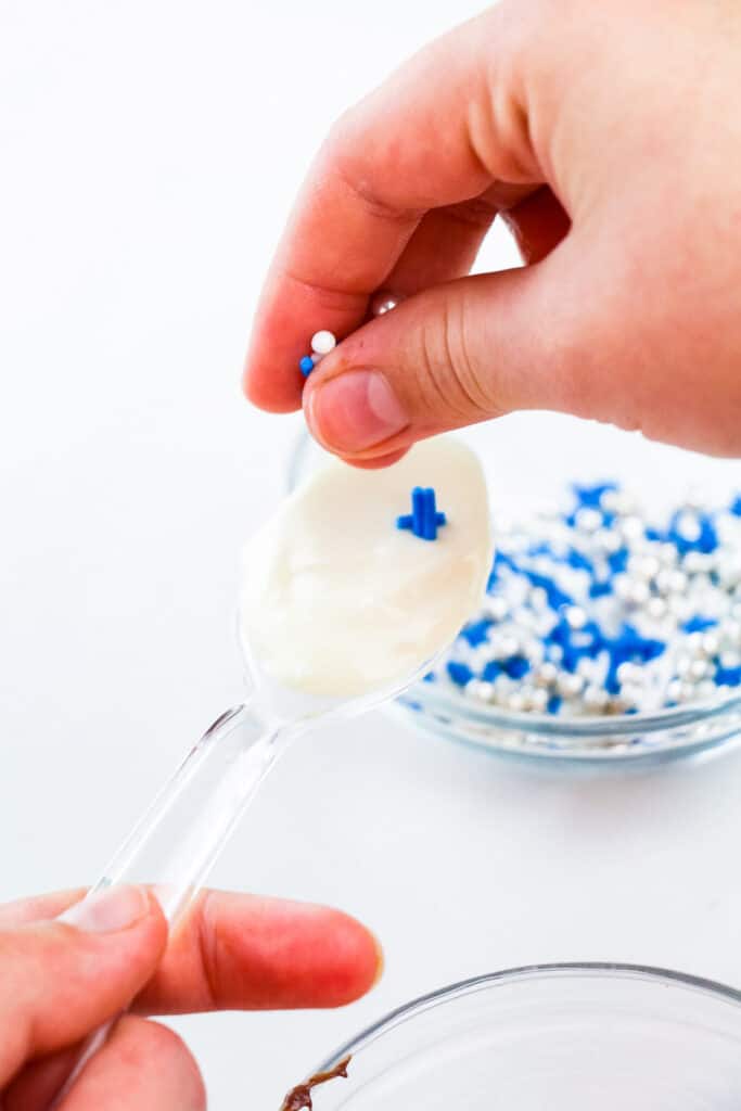 Hand putting sprinkles on a spoon covered in white chocolate