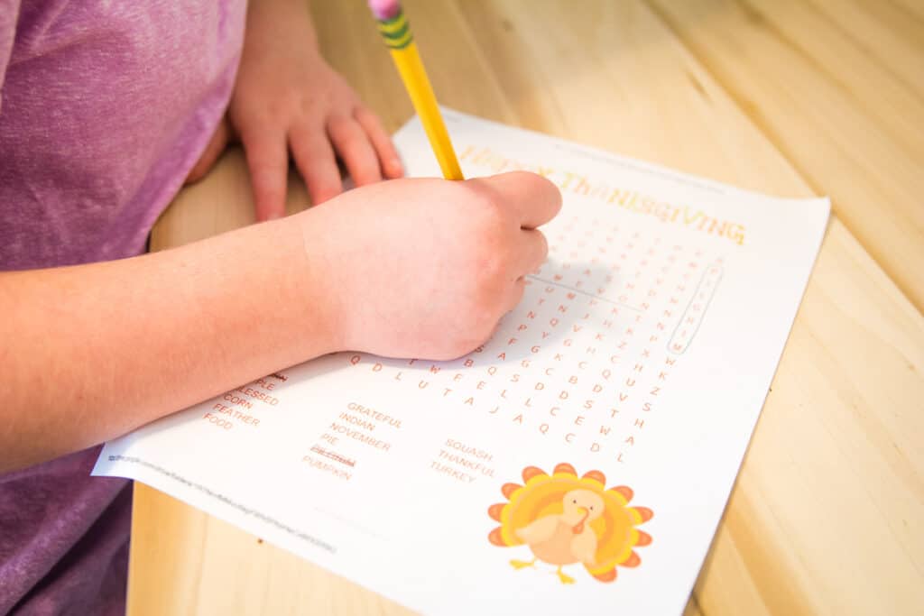 Girl working on Thanksgiving Word Find on a wooden background