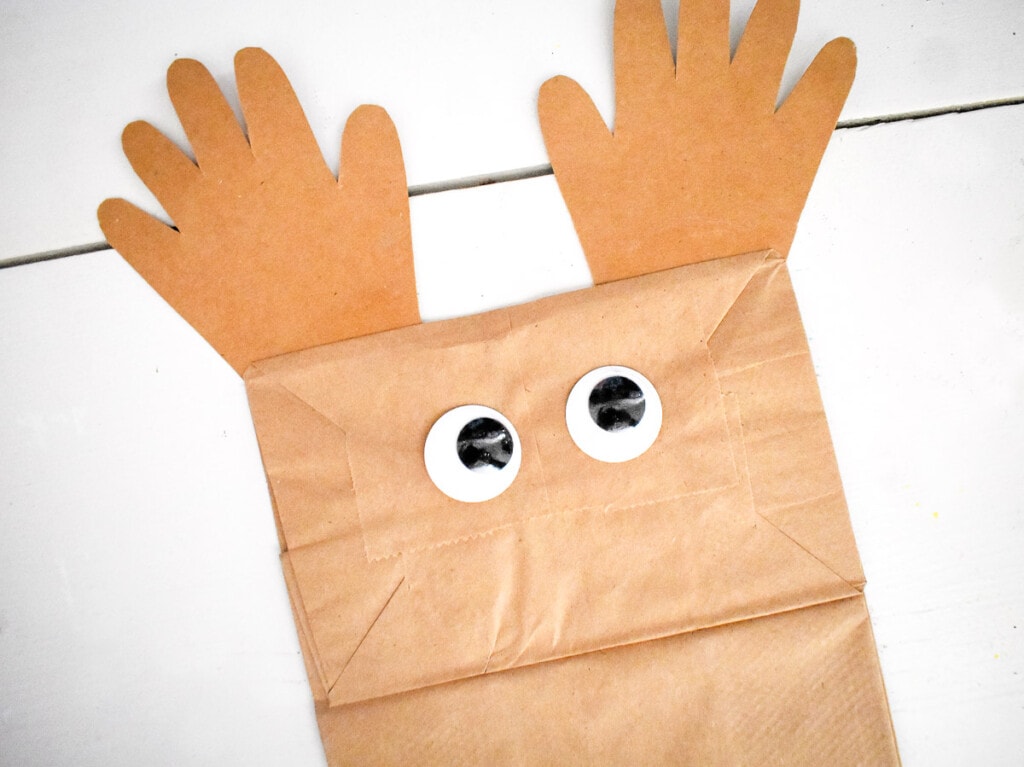 Brown paper bag with googly eyes and handprints glued to the top of it