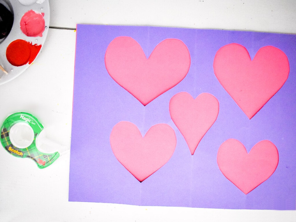 Purple paper with hearts cut out over pink paper