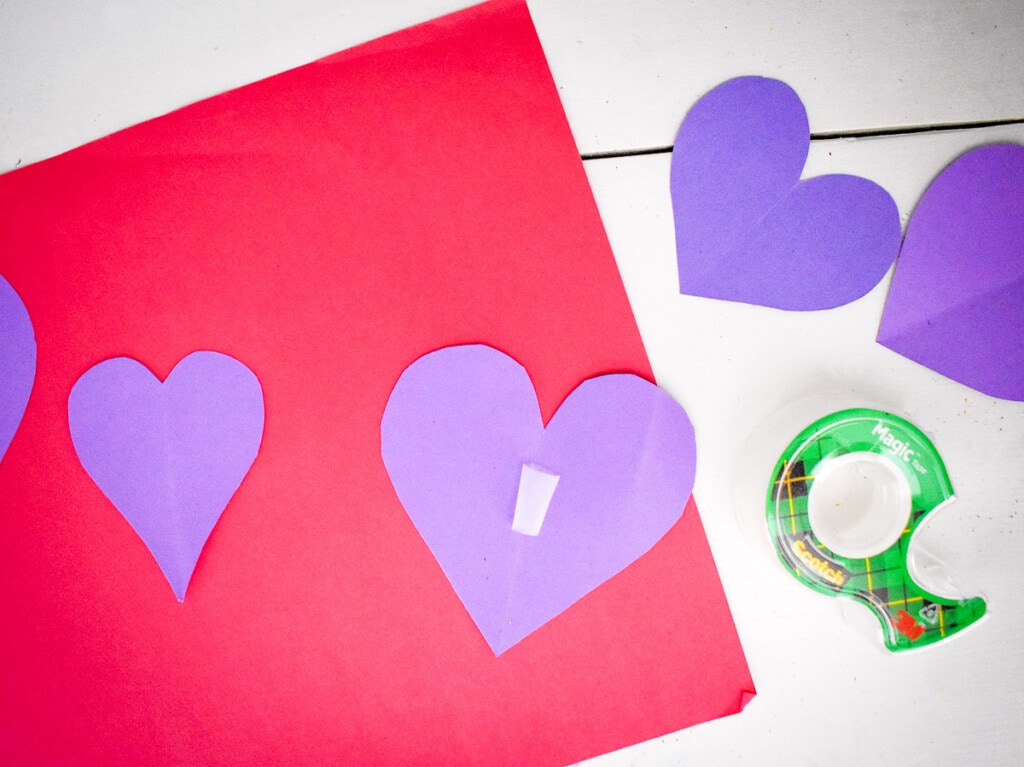 Purple hearts with tape on the back on a red piece of paper