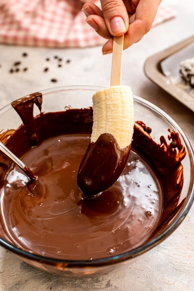 Dipping half of a banana into melted chocolate