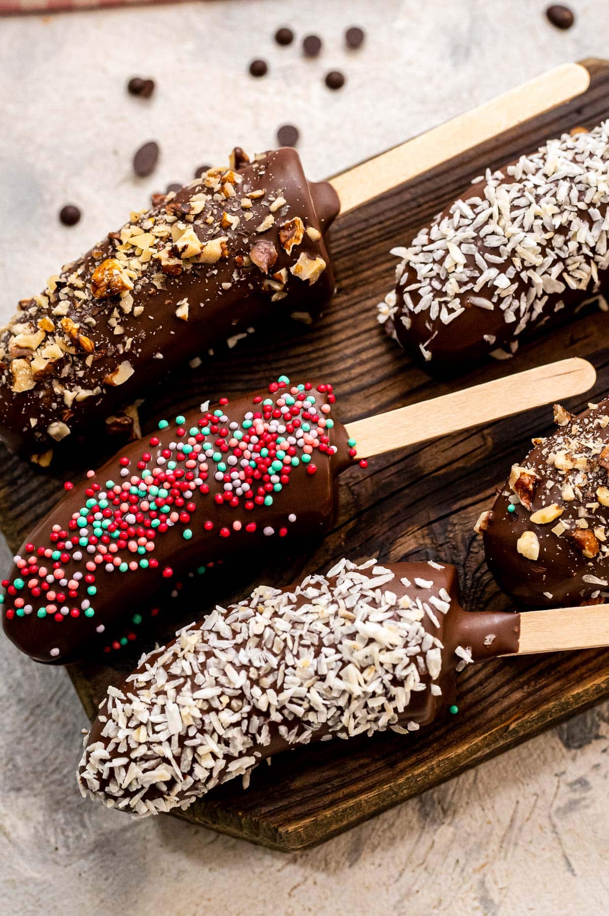 Chocolate Covered Frozen Bananas on popsicle sticks with toppings