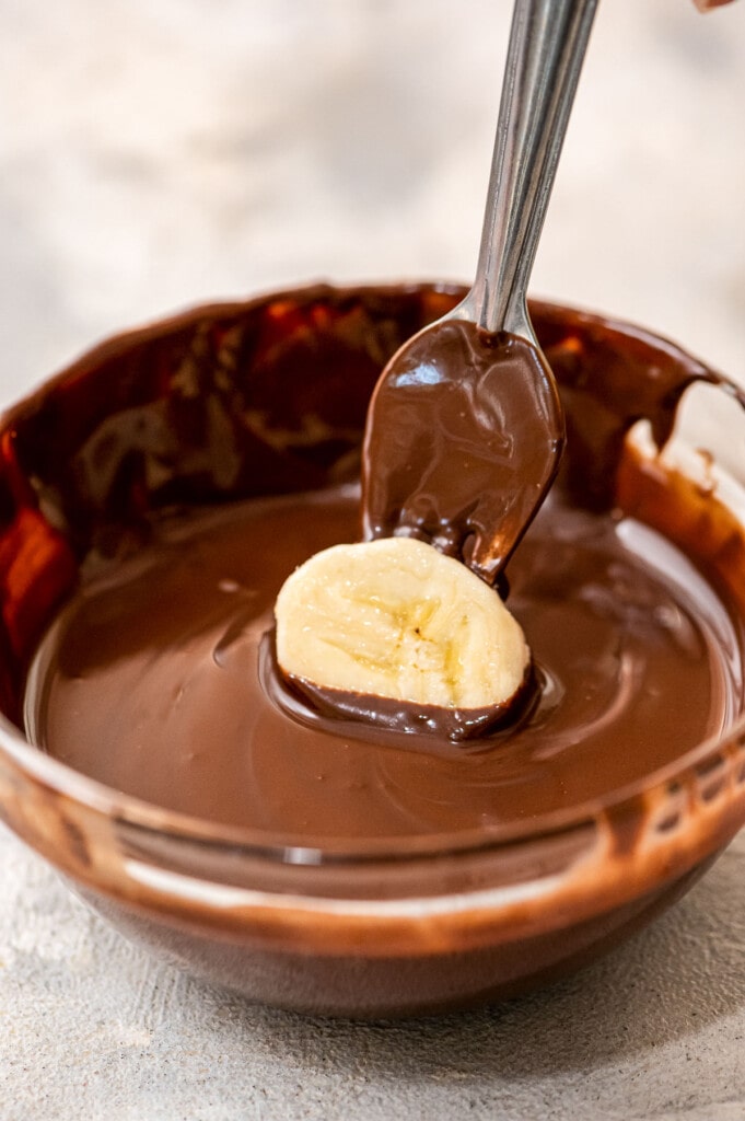 Fork dipping banana piece in melted chocolate