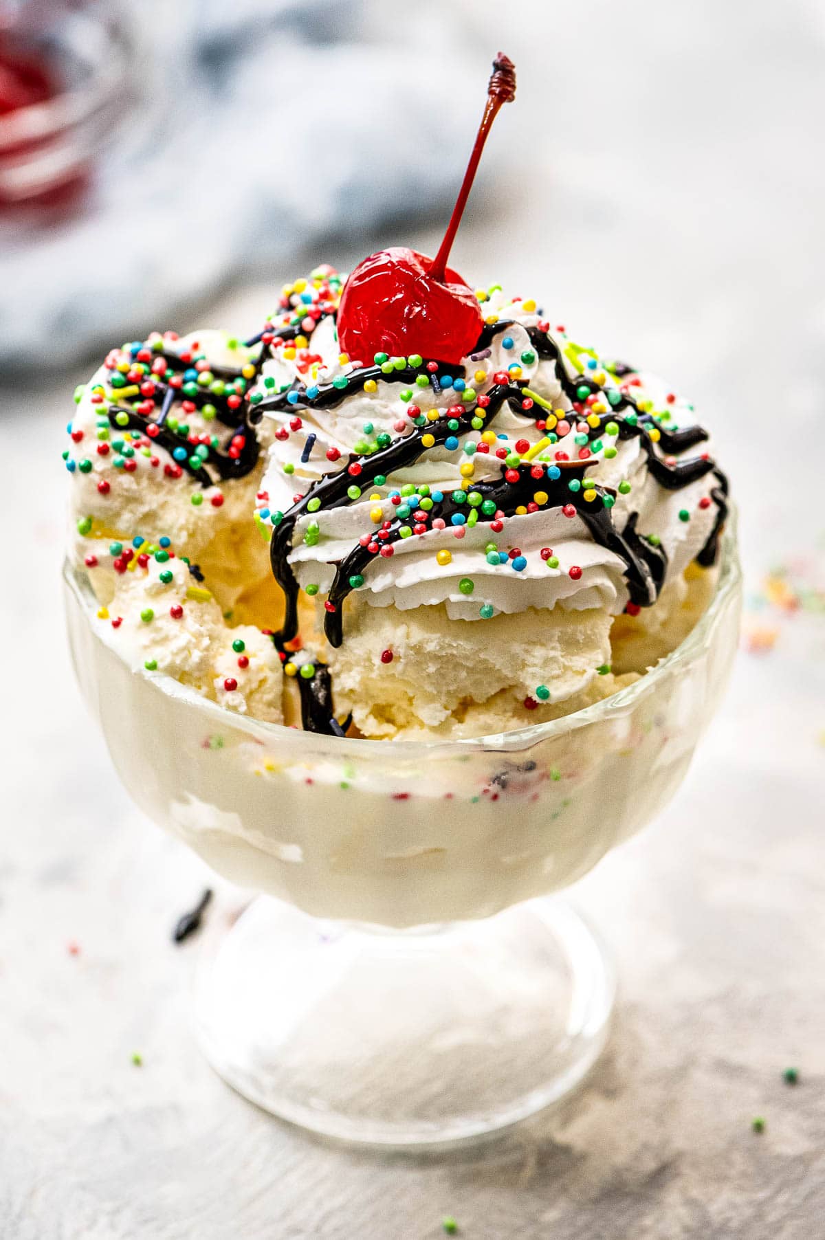 Glass bowl with ice cream, chocolate syrup, sprinkles and cherry on top