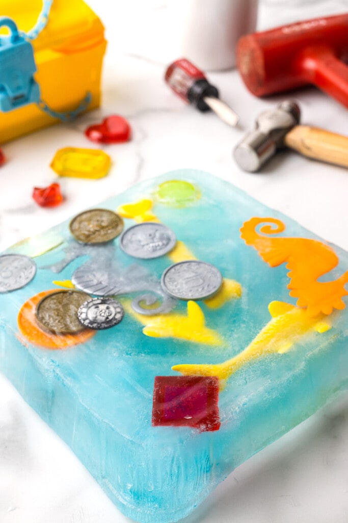 Square block of blue ice with plastic toys