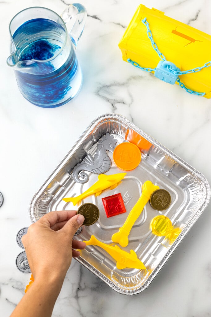 Hand putting plastic toys into a square aluminum foil pan