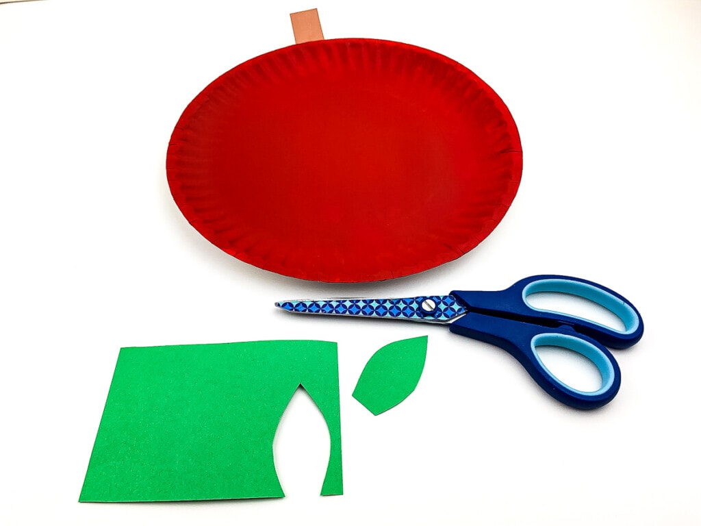 Green paper stem cut out laying with scissors and red paper plate