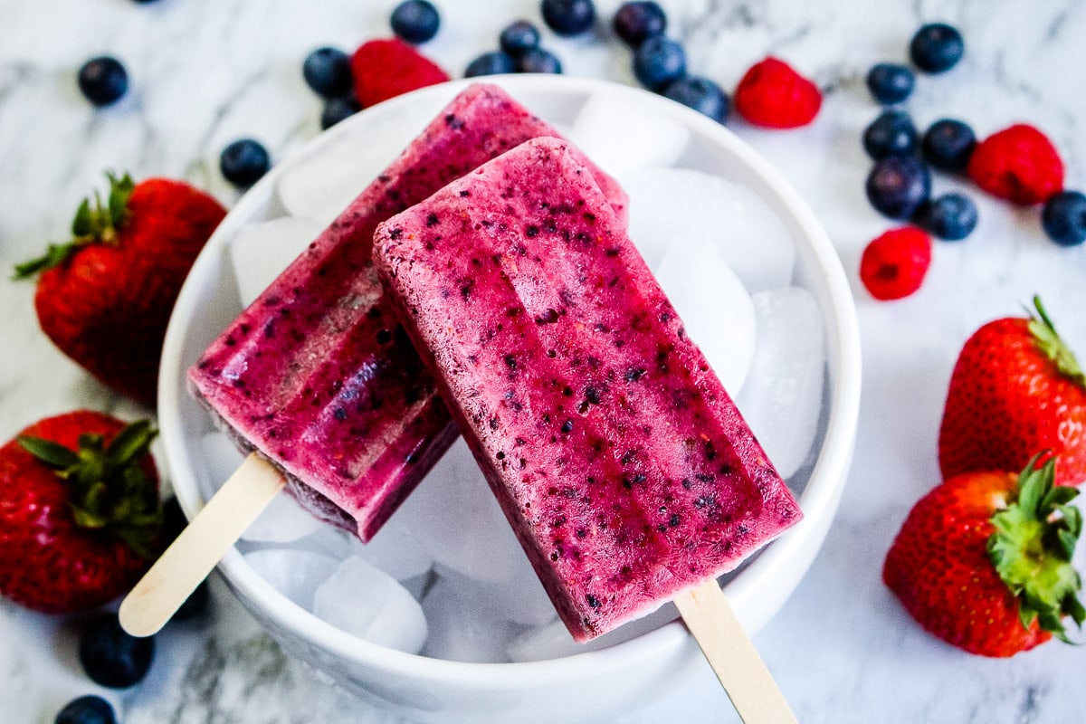 Two mixed berry popsicles laying on a bowl of ice