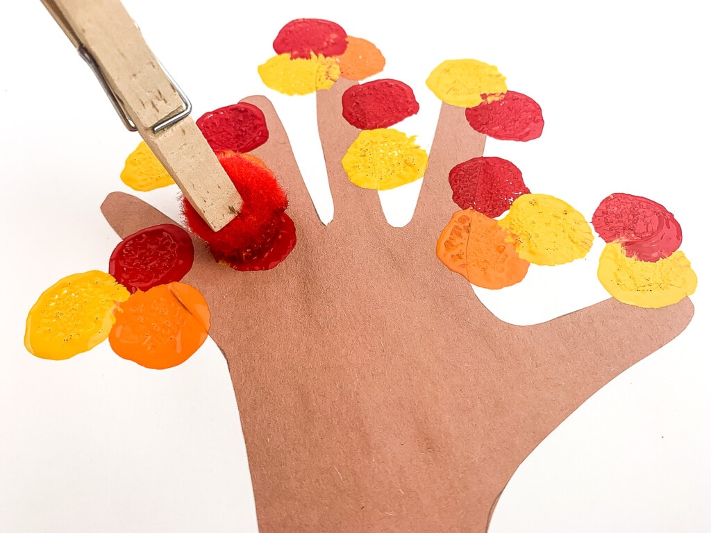 Clothespin with pom pom making dabs of paint on childs handprint tree