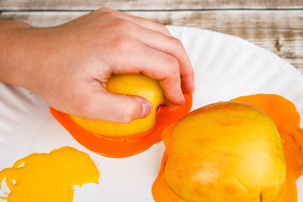 Toddlers hand pushing sliced apple onto orange paint