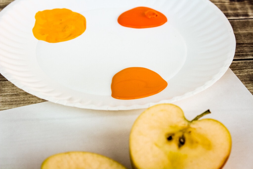 Paper plate with orange and yellow paint and cut open apple