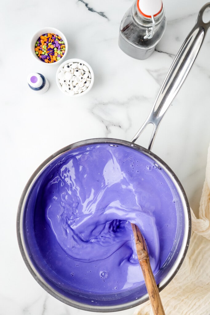 Overhead image of stirring purple food coloring into white hot chocolate in saucepan