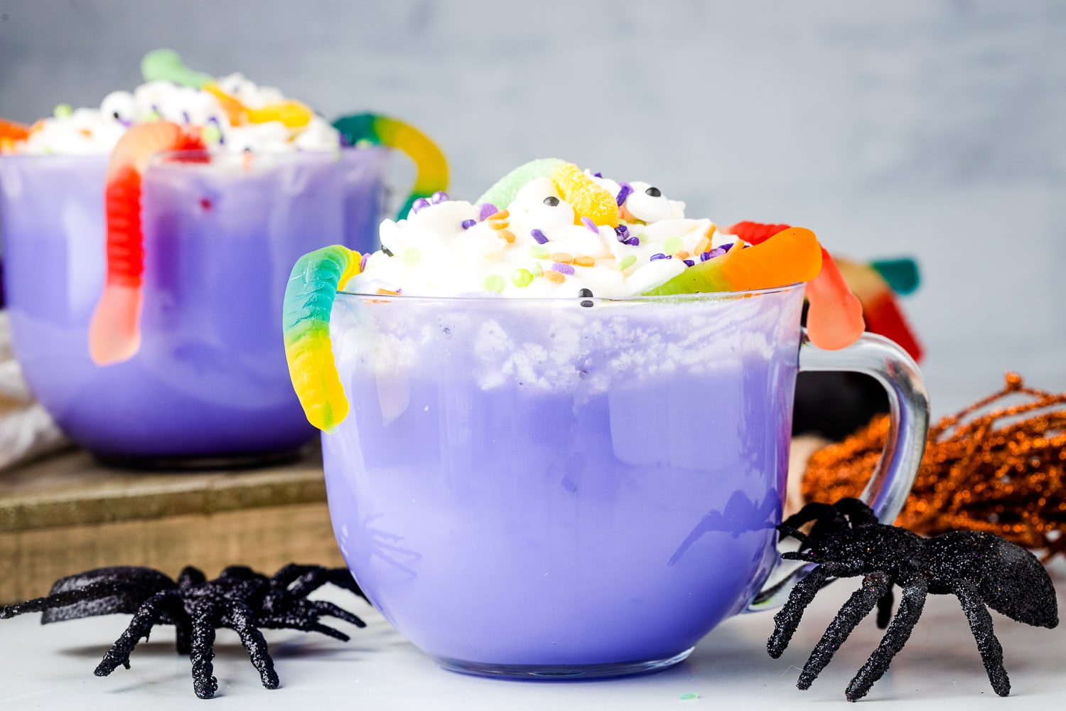 Purple hot chocolate in glass mug topped with whipped cream, sprinkles and gummy worms