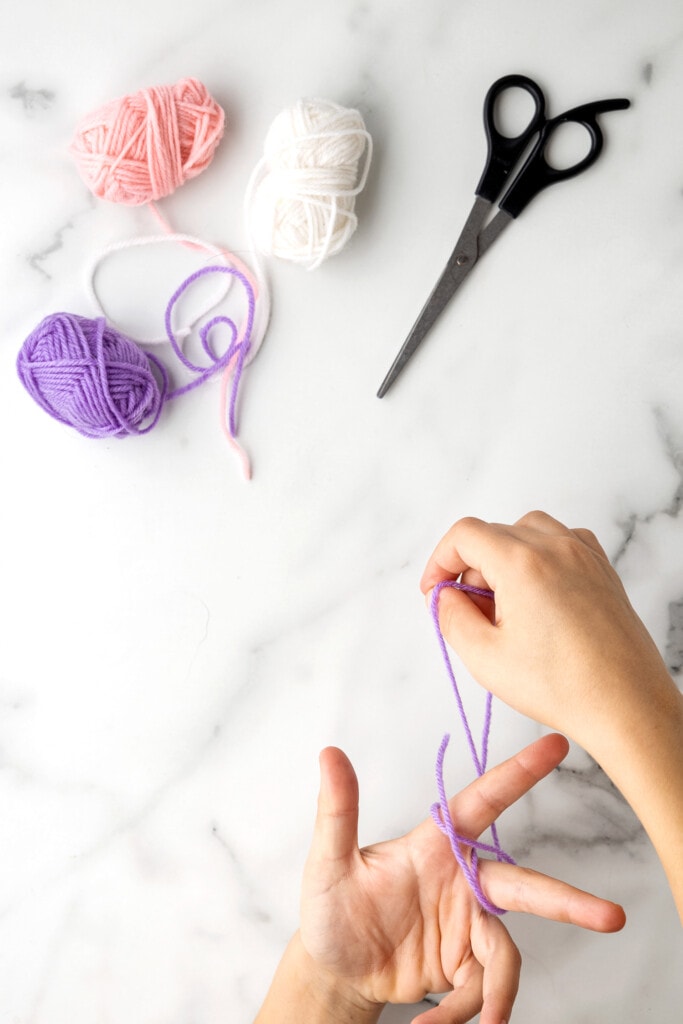 Weaving yarn to make butterfly craft on fingers