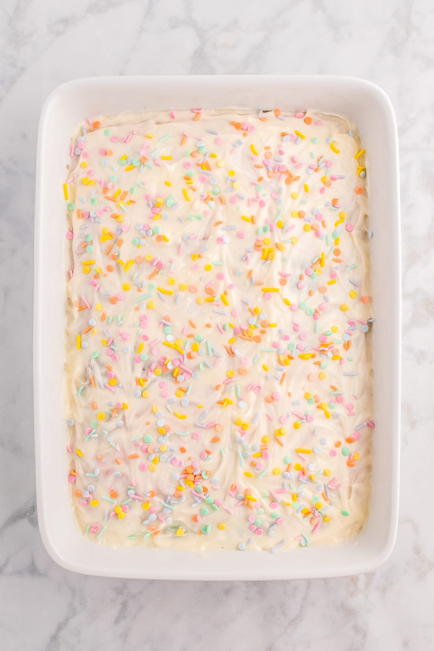 Overhead image of white frosted cake with pastel sprinkles