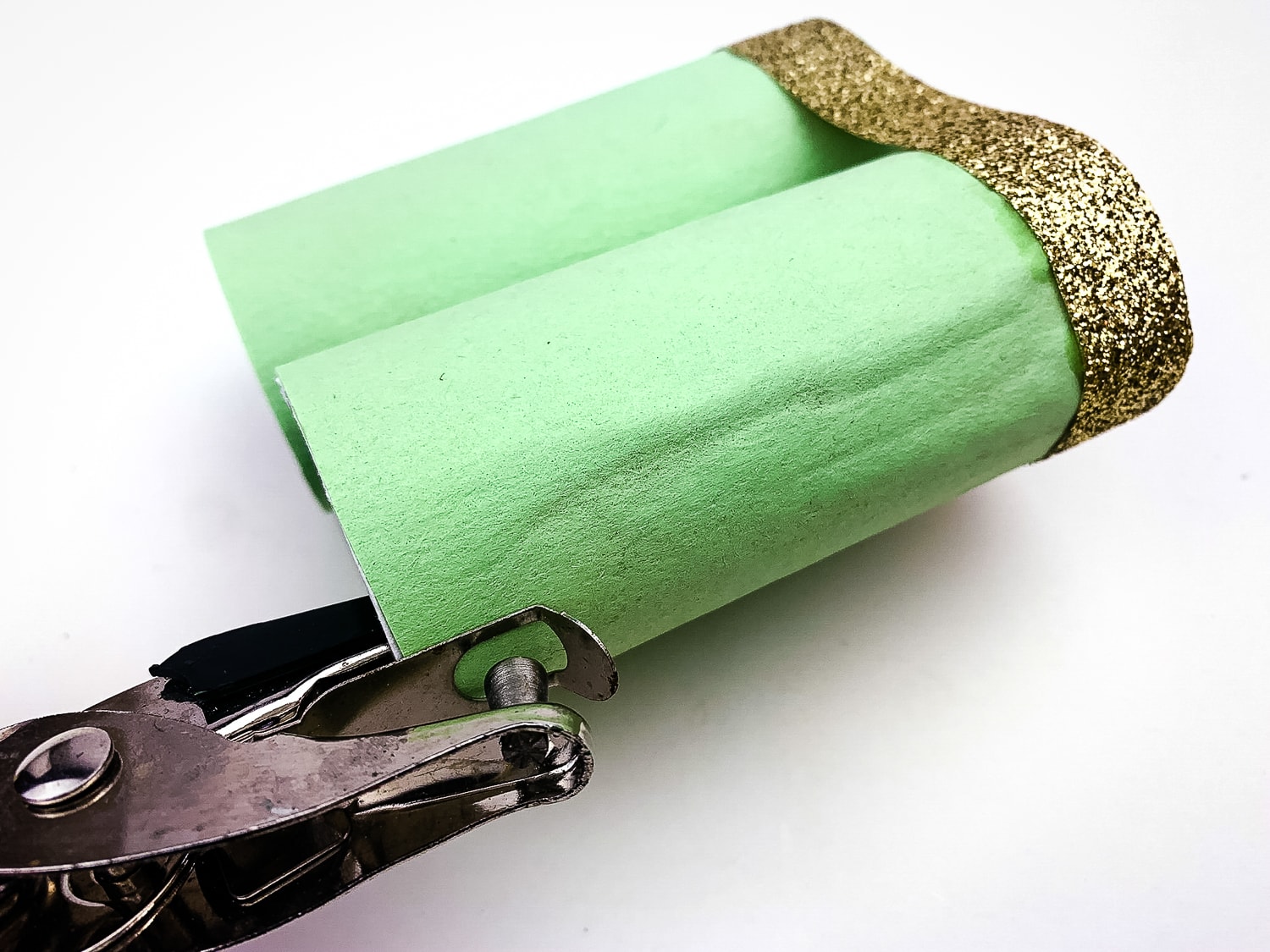 Punching hole in green paper covered toilet paper roll