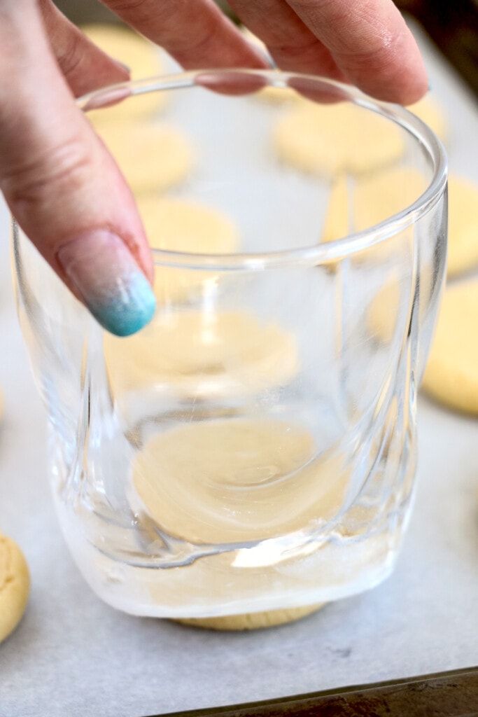 Hand pressing a glass down on sugar cookie dough ball