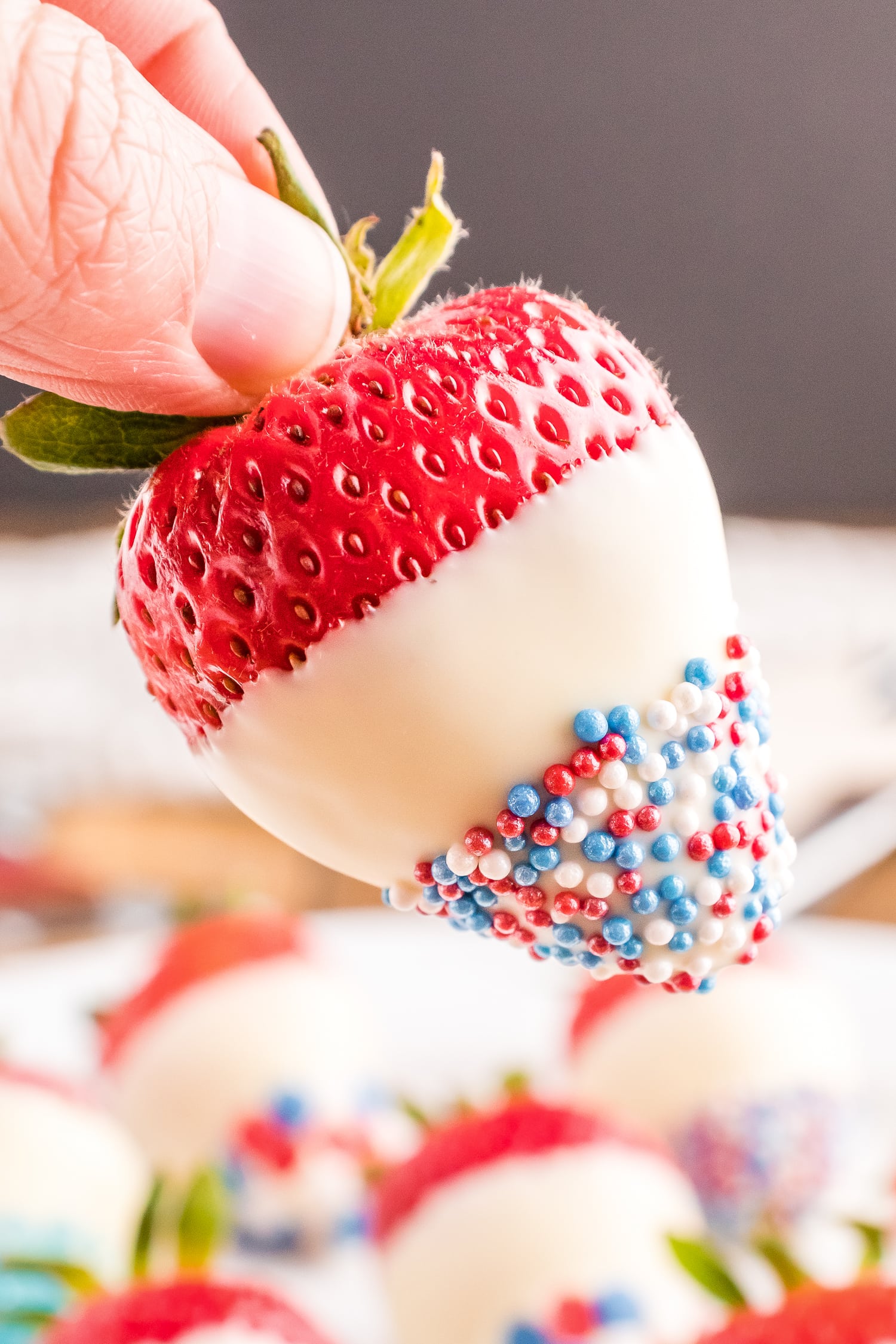 Hand holding strawberry dipped in white chocolate and patriotic sprinkles