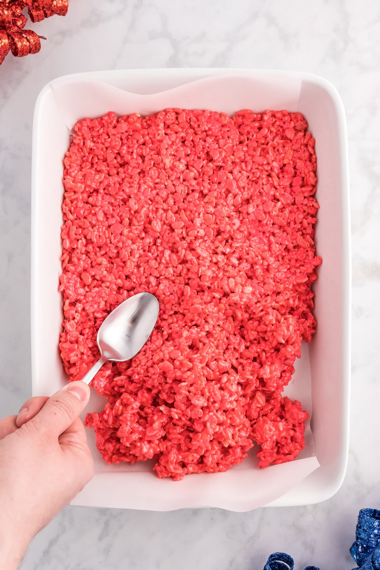 Spreading red rice krispie treats on bottom of pan