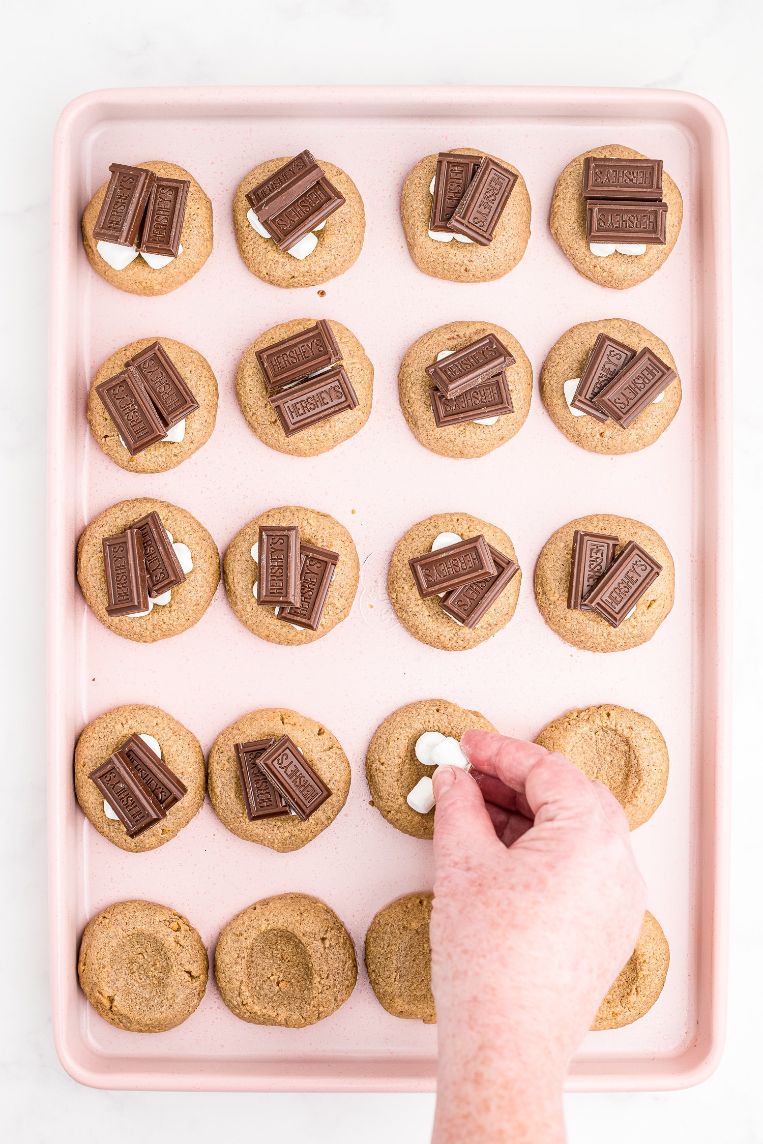 Hand placing chocolate bars on top of cookies.
