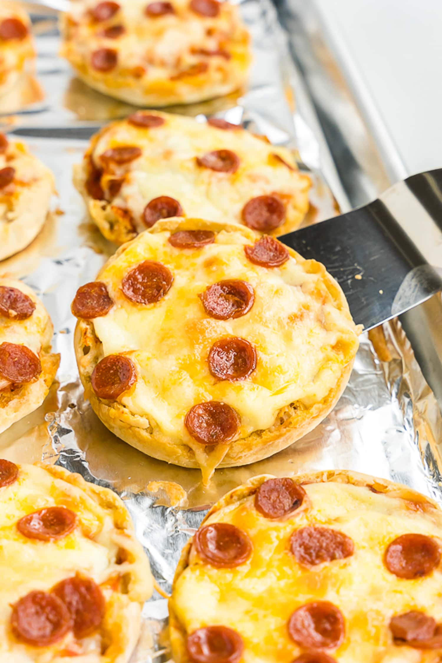 Spatula lifting an Baked English Muffin Pizza off baking sheet