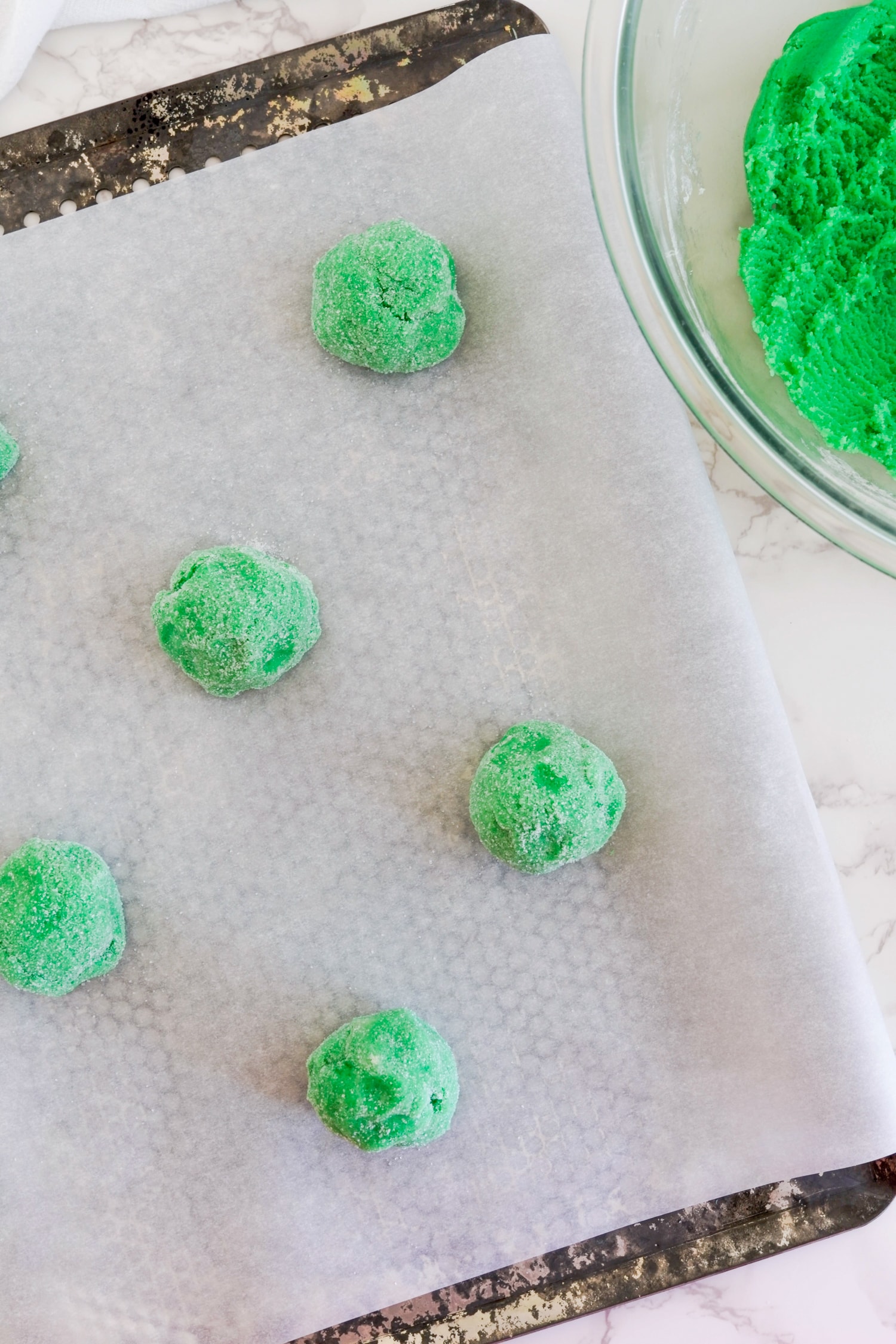 Green sugar cookie dough balls on parchment lined baking sheet