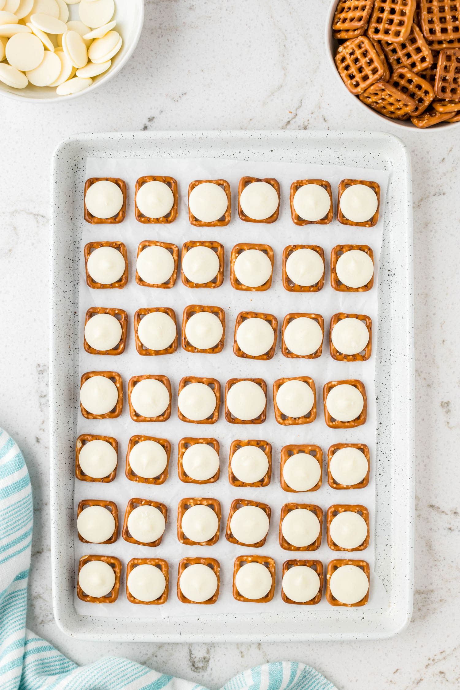 Laying Square Pretzels on a Cookie Sheet with a Candy Melt On Top of Each Pretzel