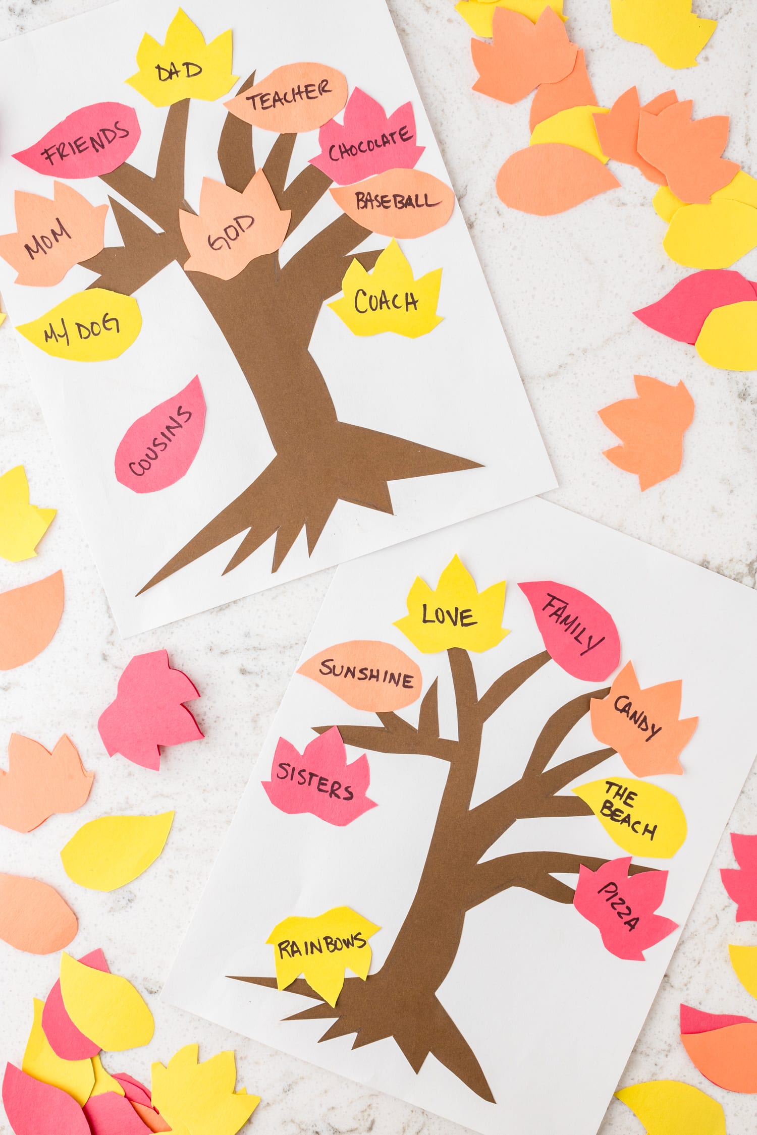 Two Completed Thankful Tree Crafts with leaves laying all around it.