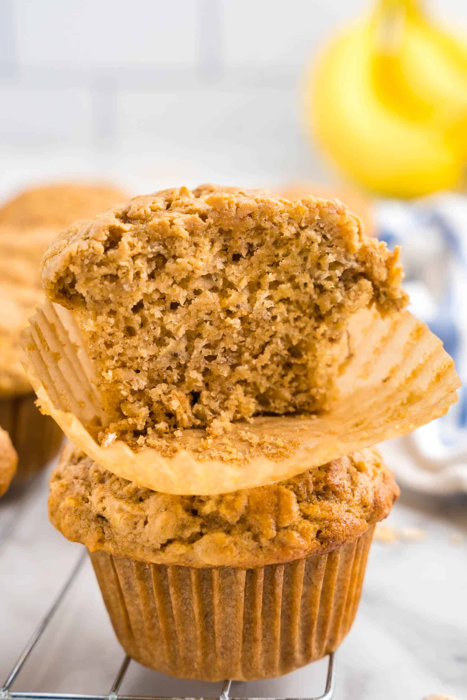 Two Banana muffins stacked on top of each other and the to one is cut in half to show the fluffy inside.