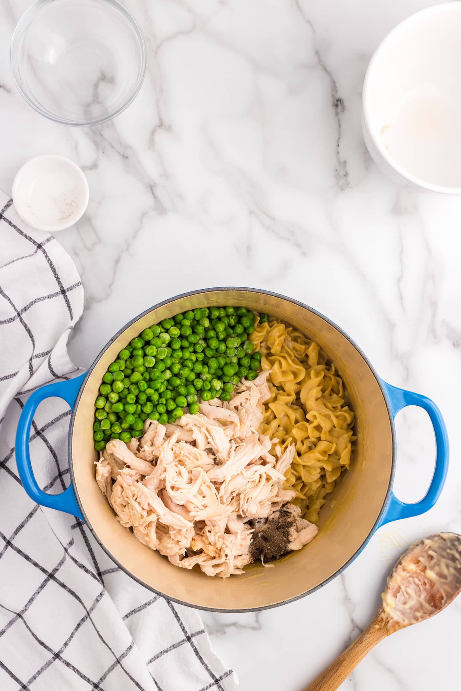 Adding frozen peas and shredded chicken to Chicken and Noodles recipe in stovetop pot