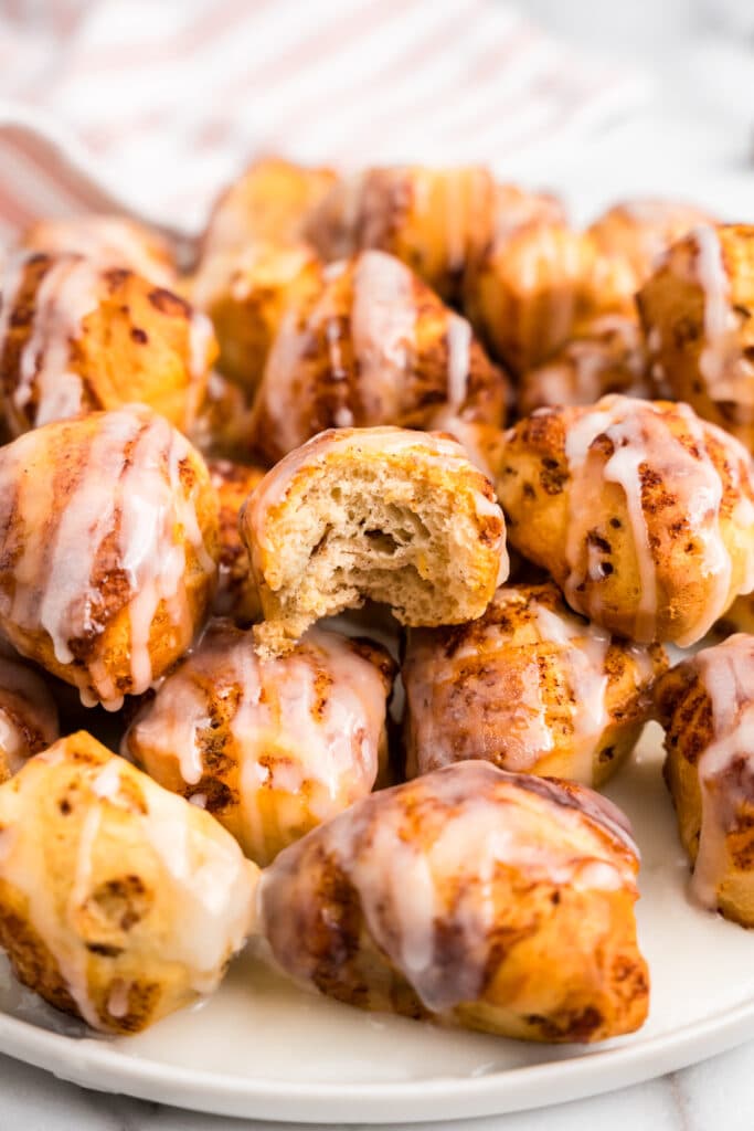 A pile of cinnamon roll bites on a white plate with a bite taken out of one of them.