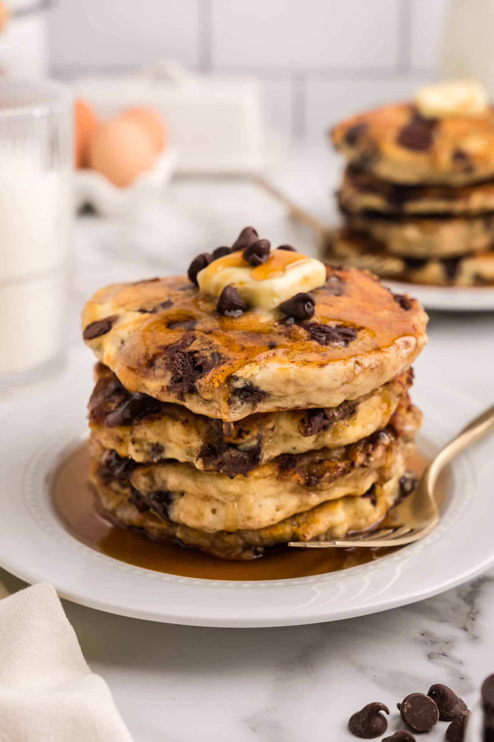 A stack of pancakes on a white plate with butter and syrup on top.