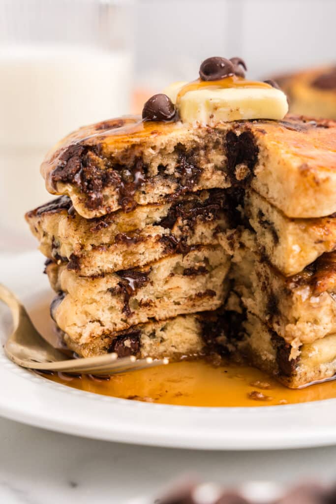 A stack of pancakes on a white plate with a big piece cut out to show the inside fluffiness of the pancakes.
