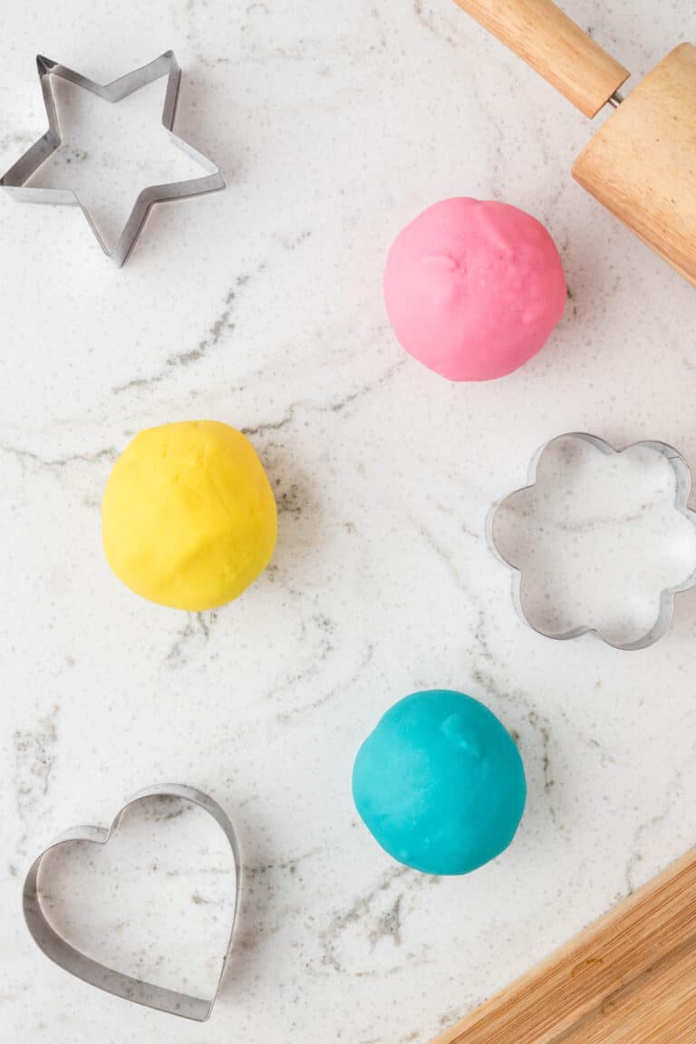 Three color rolls of microwave playdough with cookie cutters beside them and rolling pins.