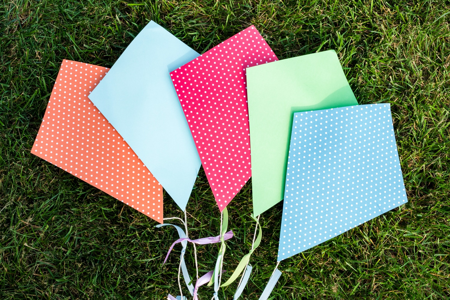 Paper Kite Crafts made with a variety of cardstock and tail ribbons arranged in the grass