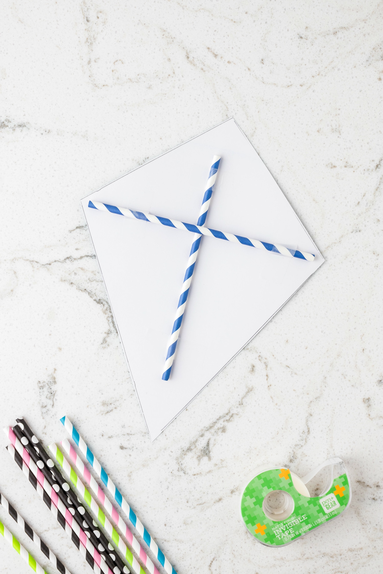 Criss crossing two straws on the backside of the kite and using transparent tape to adhere for the Paper Kite Craft