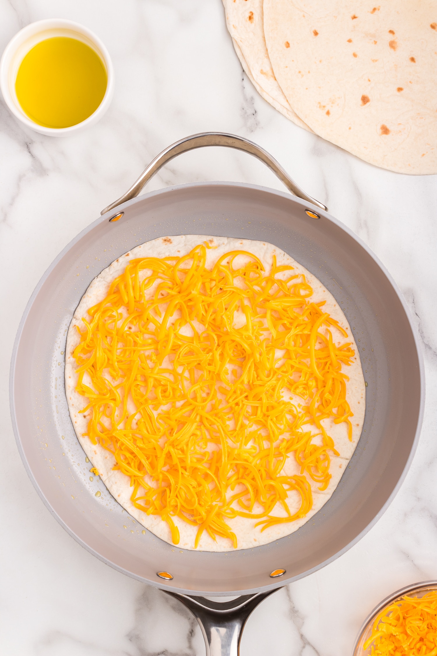 Large tortilla layered with shredded cheese in stovetop skillet for Cheese Quesadilla