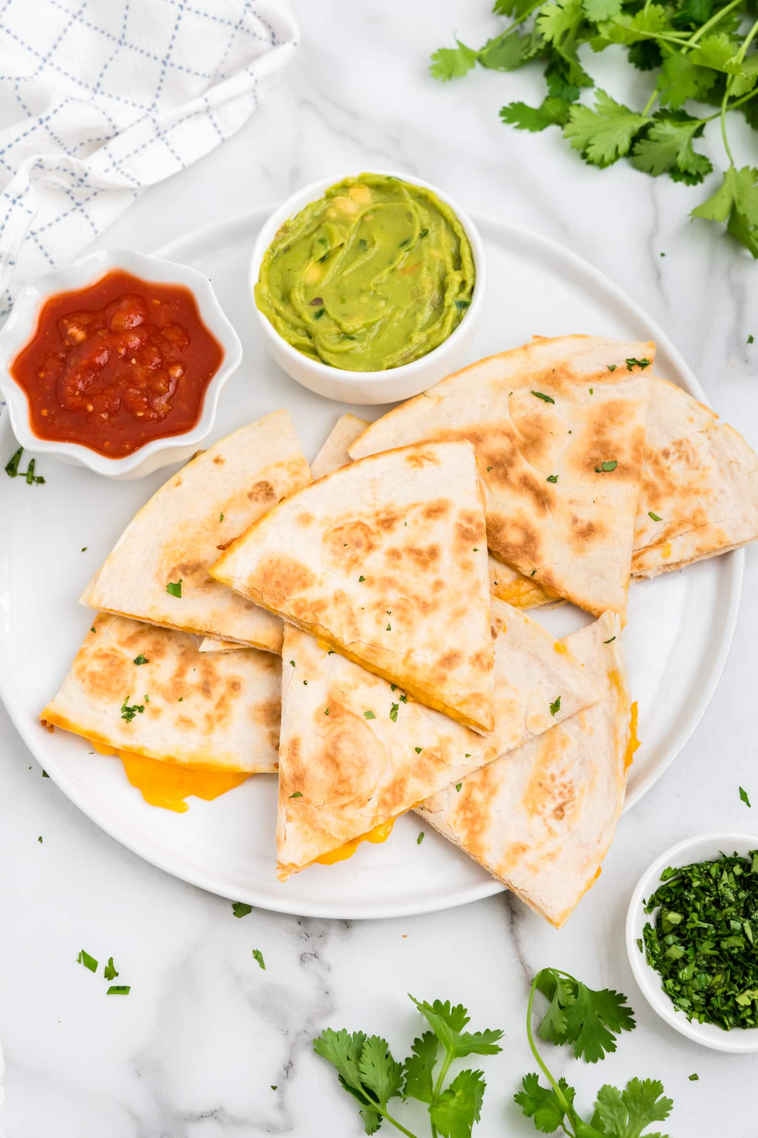 Cheese Quesadilla cut into pieces arranged on a plate with salsa and guac in dipping bowls