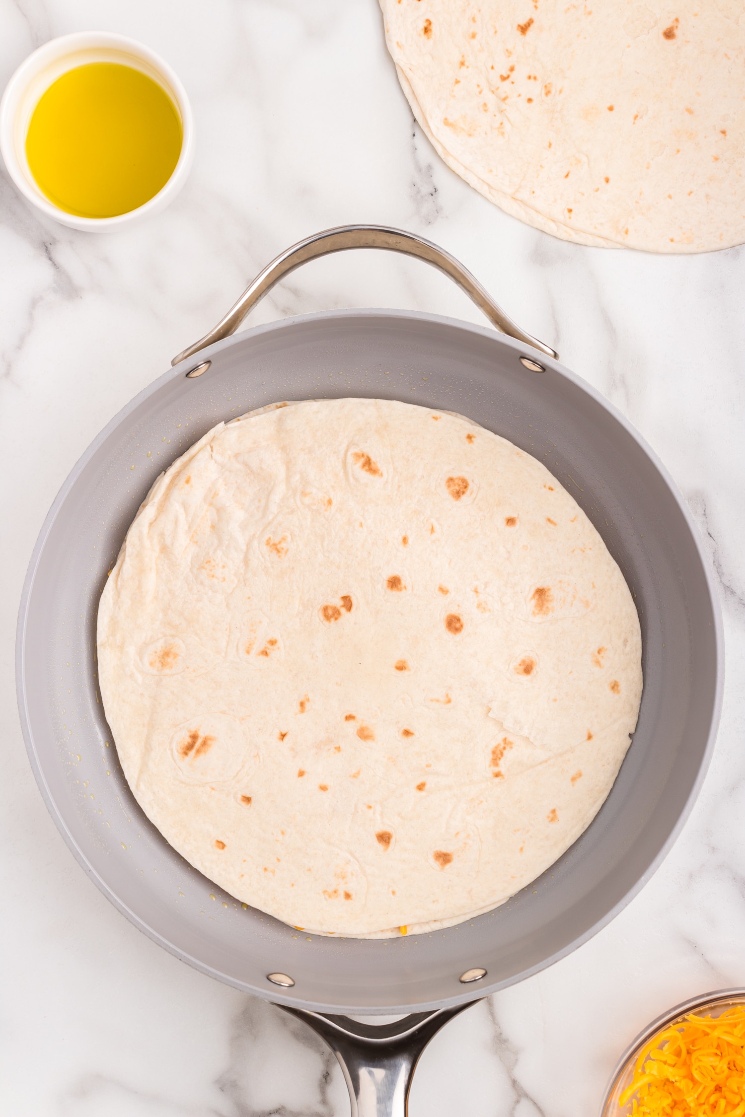 Adding another tortilla to the Cheese Quesadilla in the skillet