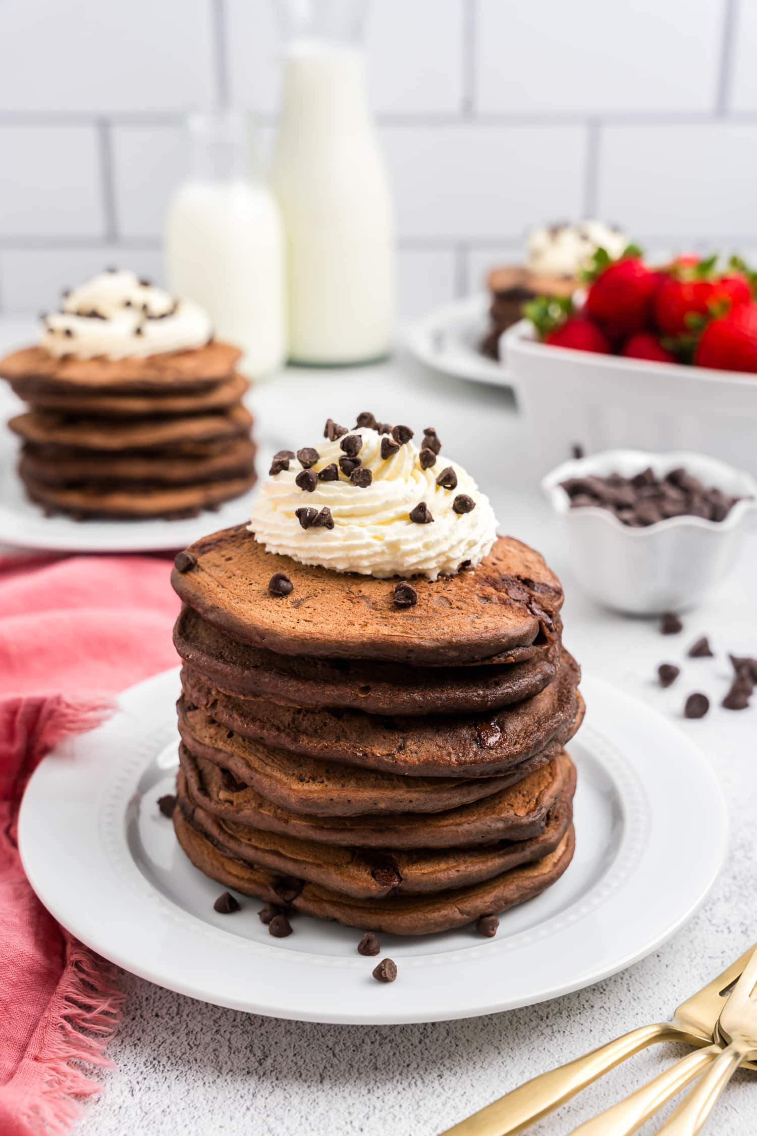 Chocolate Pancakes stacked on white plate topped with whipped cream and chocolate chips