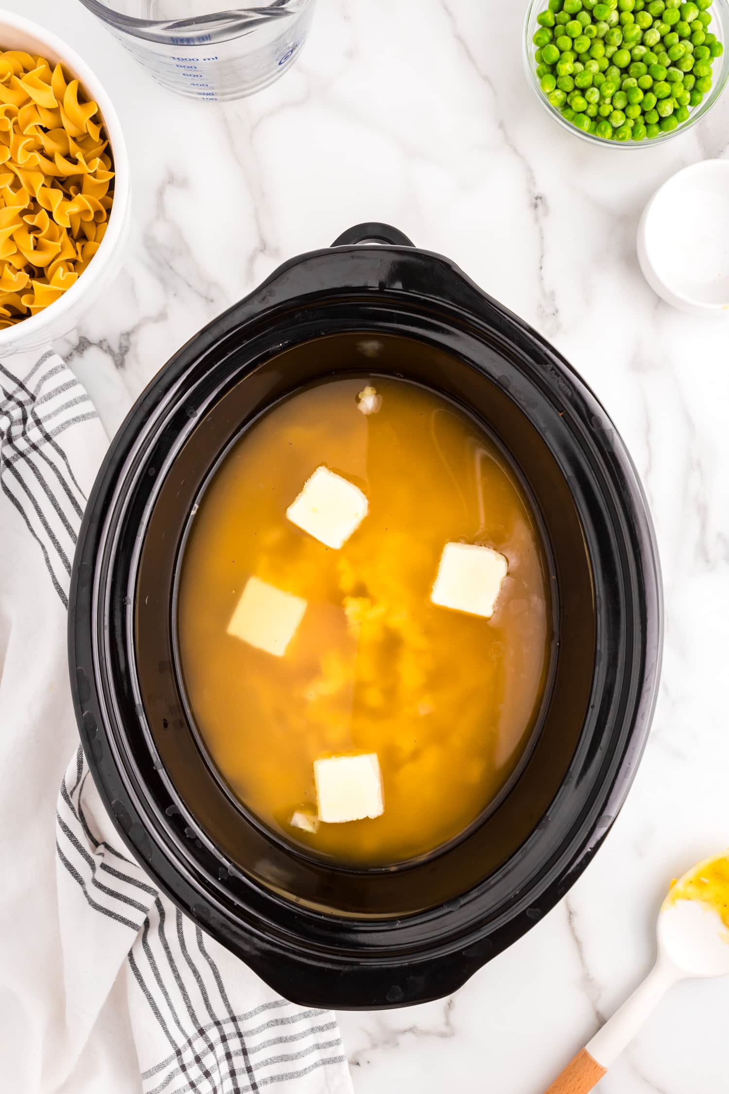 Adding broth and butter to crock pot for Crock Pot Chicken and Noodles recipe