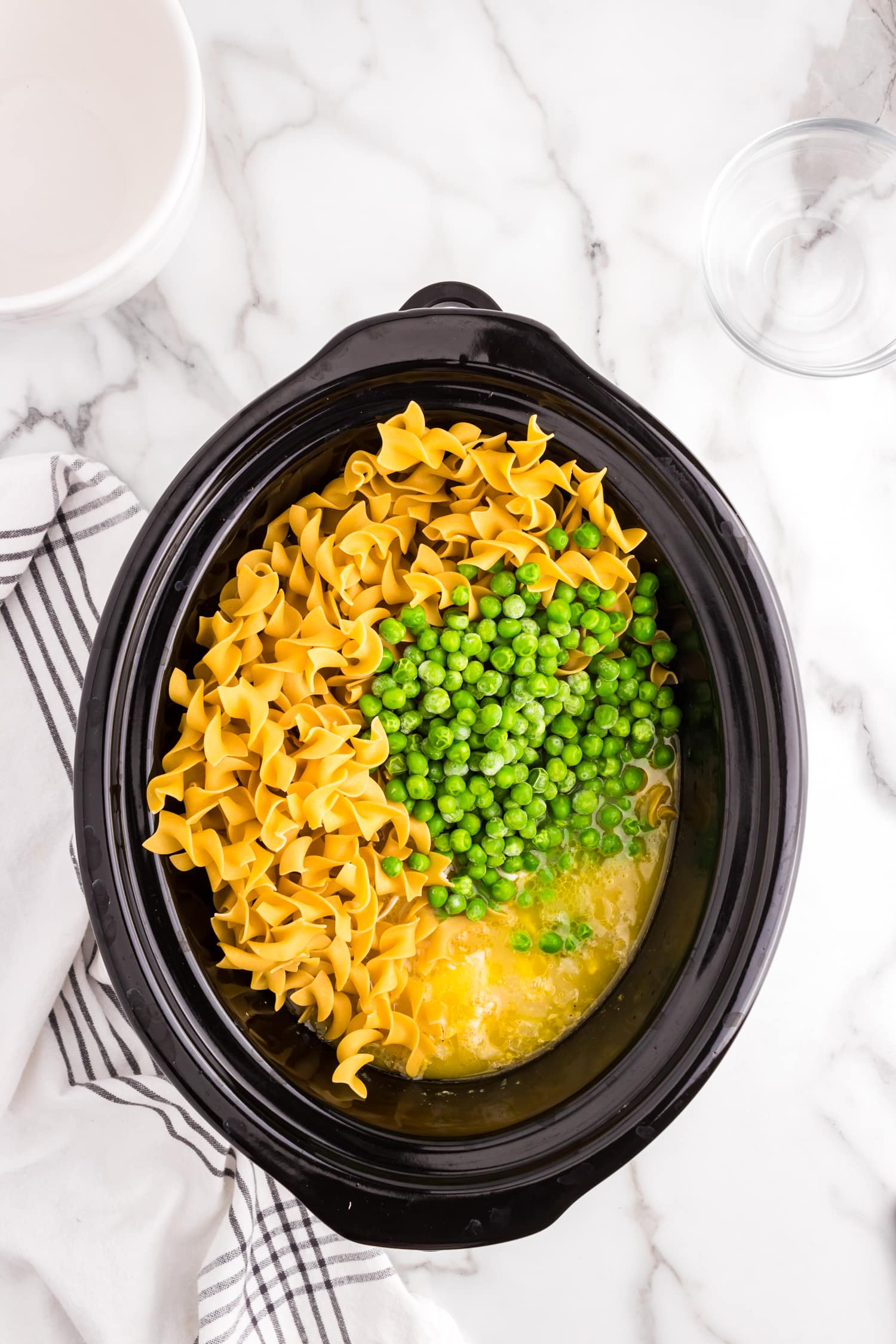 Adding egg noodles and frozen peas to Shredding chicken in crock pot mixture for Crock Pot Chicken and Noodles in crock pot