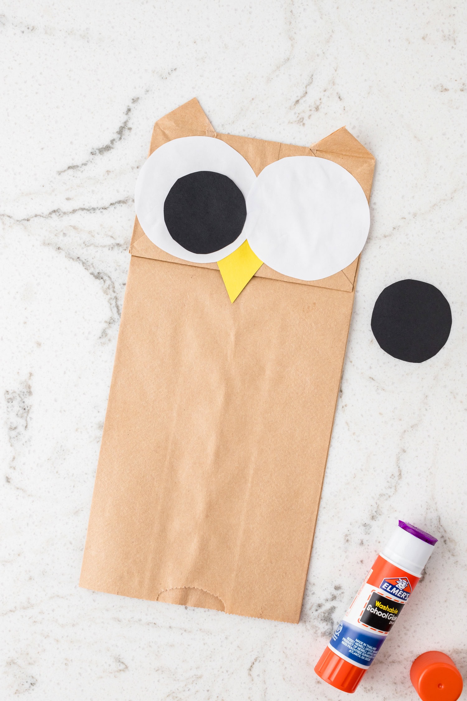 Using a glue stick to fasten the owl's eyes using white and black circles for the Paper Bag Owl Craft