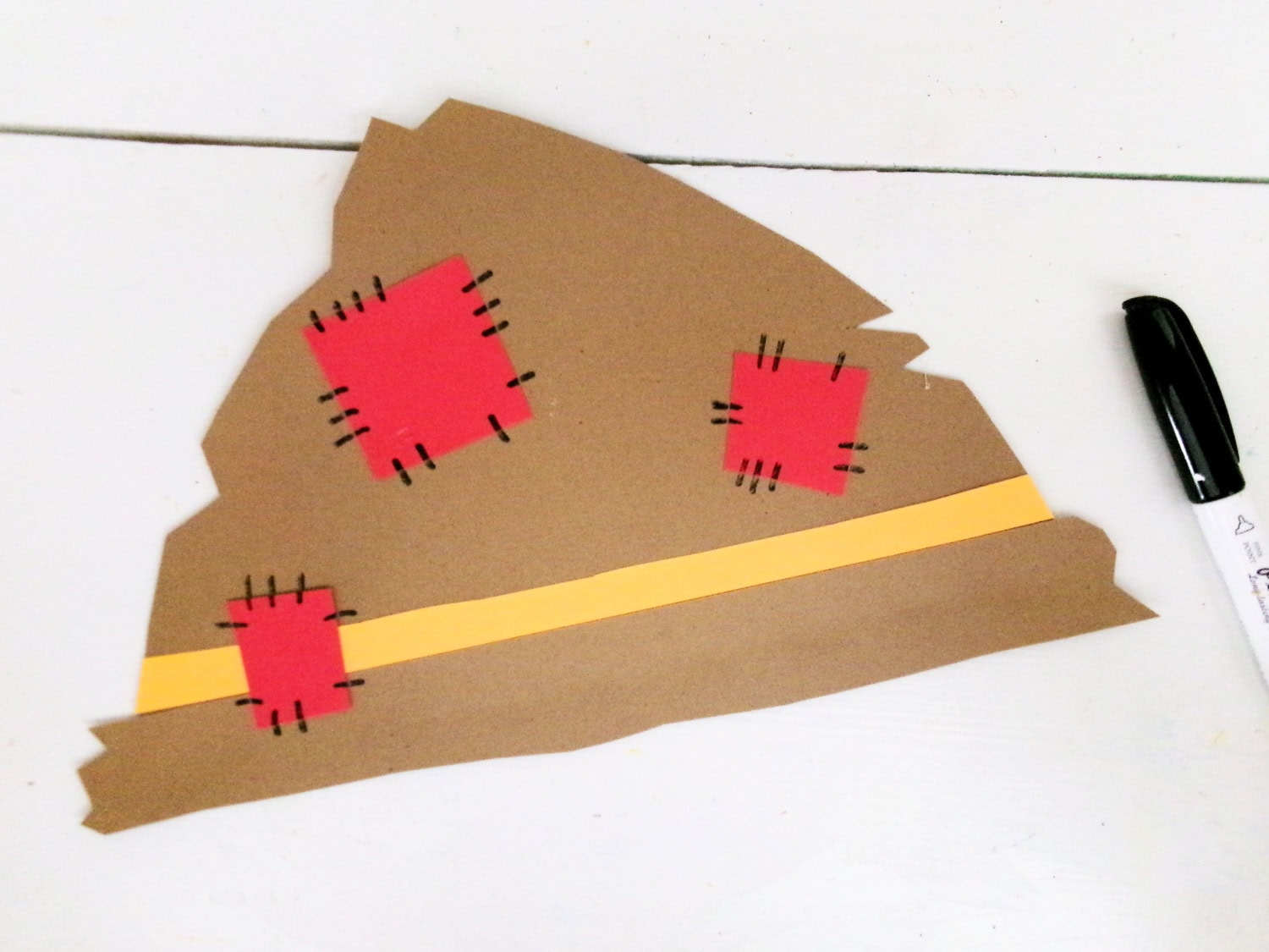 Using a black marker to add line groupings around red patches for a sewn look for the Paper Plate Scarecrow Craft