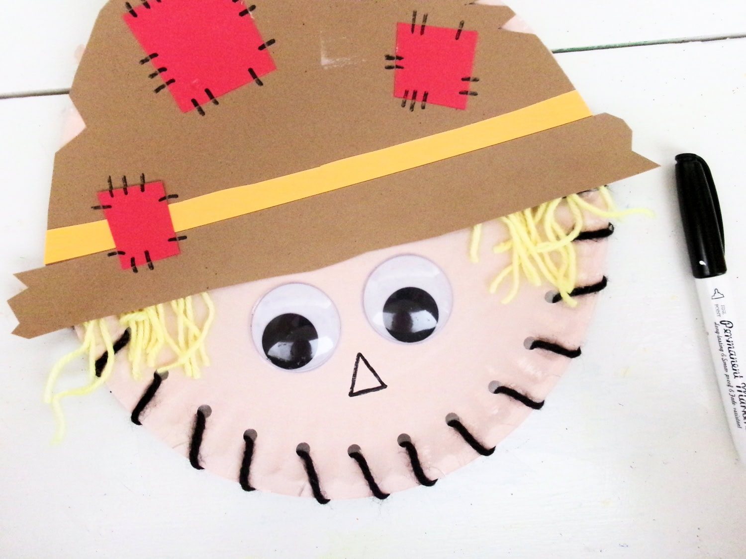 Using a black marker to drawn an upside down triagle for a nose on the Paper Plate Scarecrow Craft