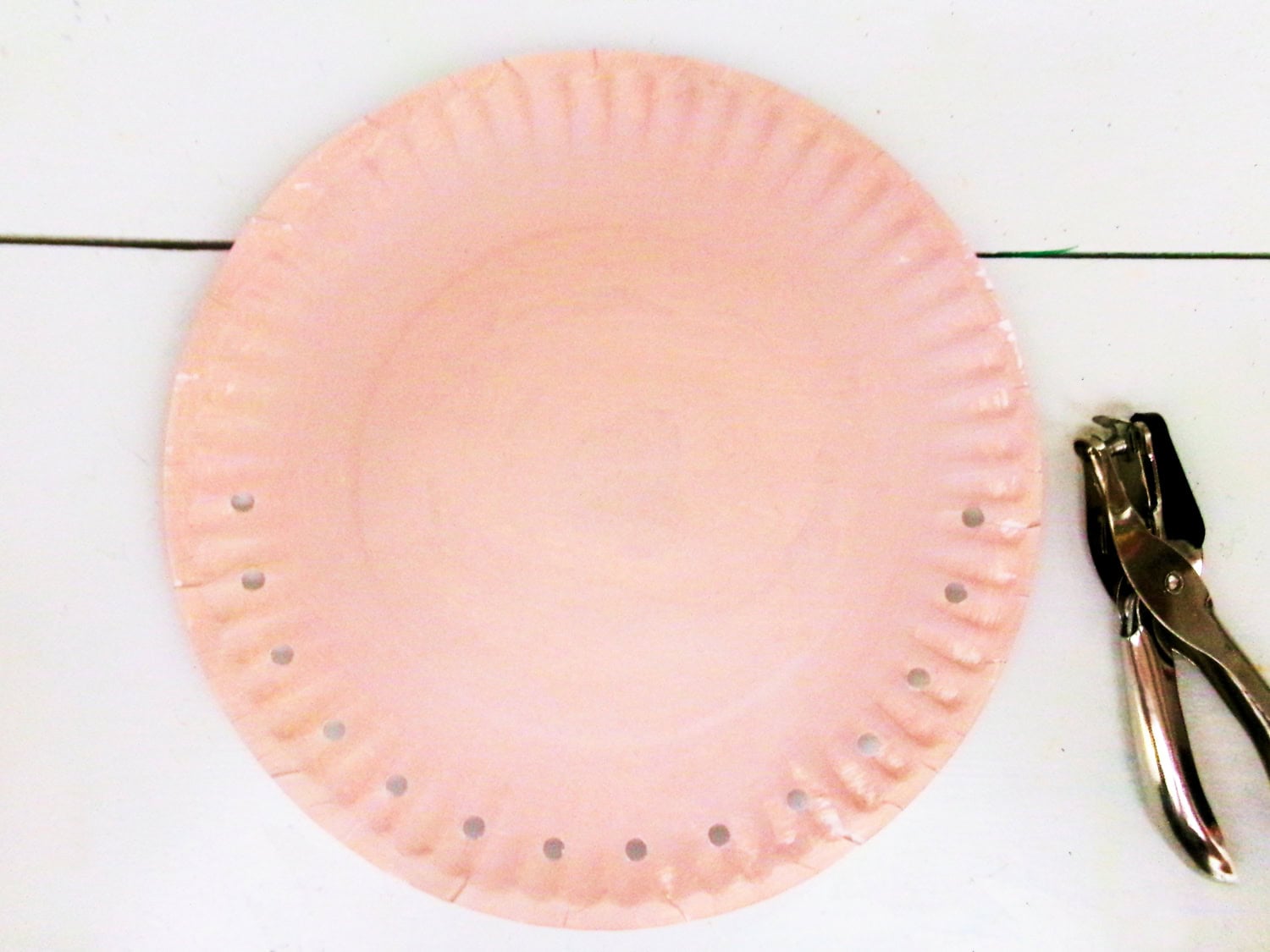 Using a single hole punch to add holes around half of the painted plate for the Paper Plate Scarecrow Craft