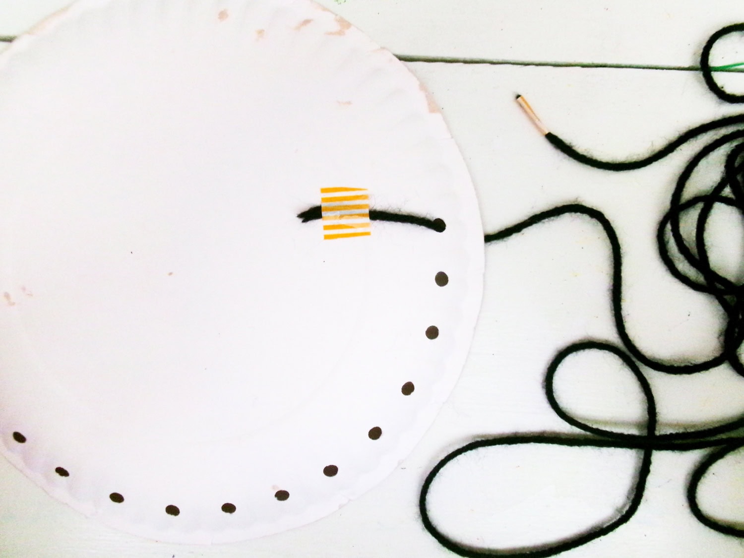 With the paper plate flipped over, the black yarn to taped to keep in place while weaving through the holes for the Paper Plate Scarecrow Craft