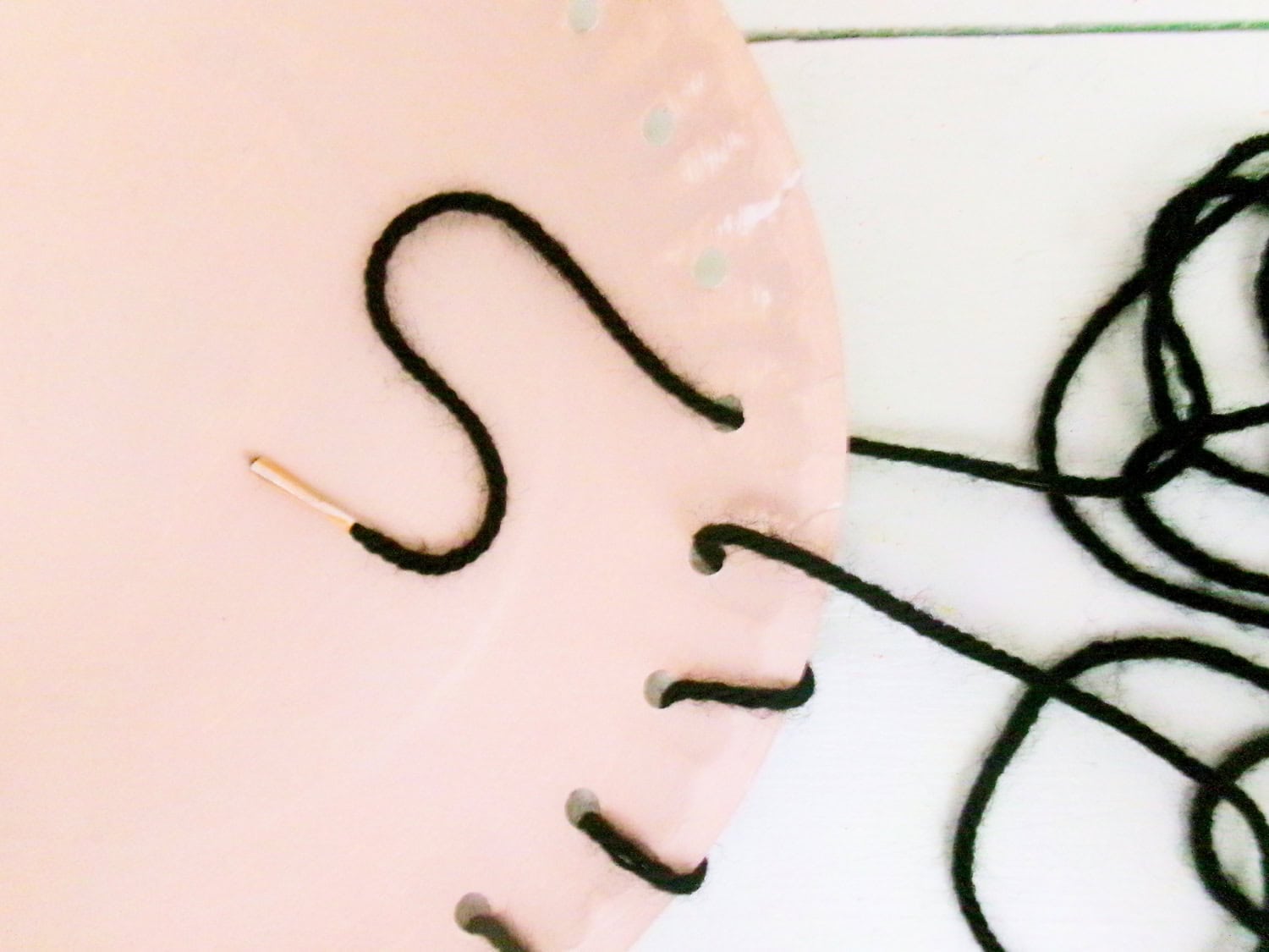 Feeding the black yarn through the punched holes of the painted plate for the Paper Plate Scarecrow Craft