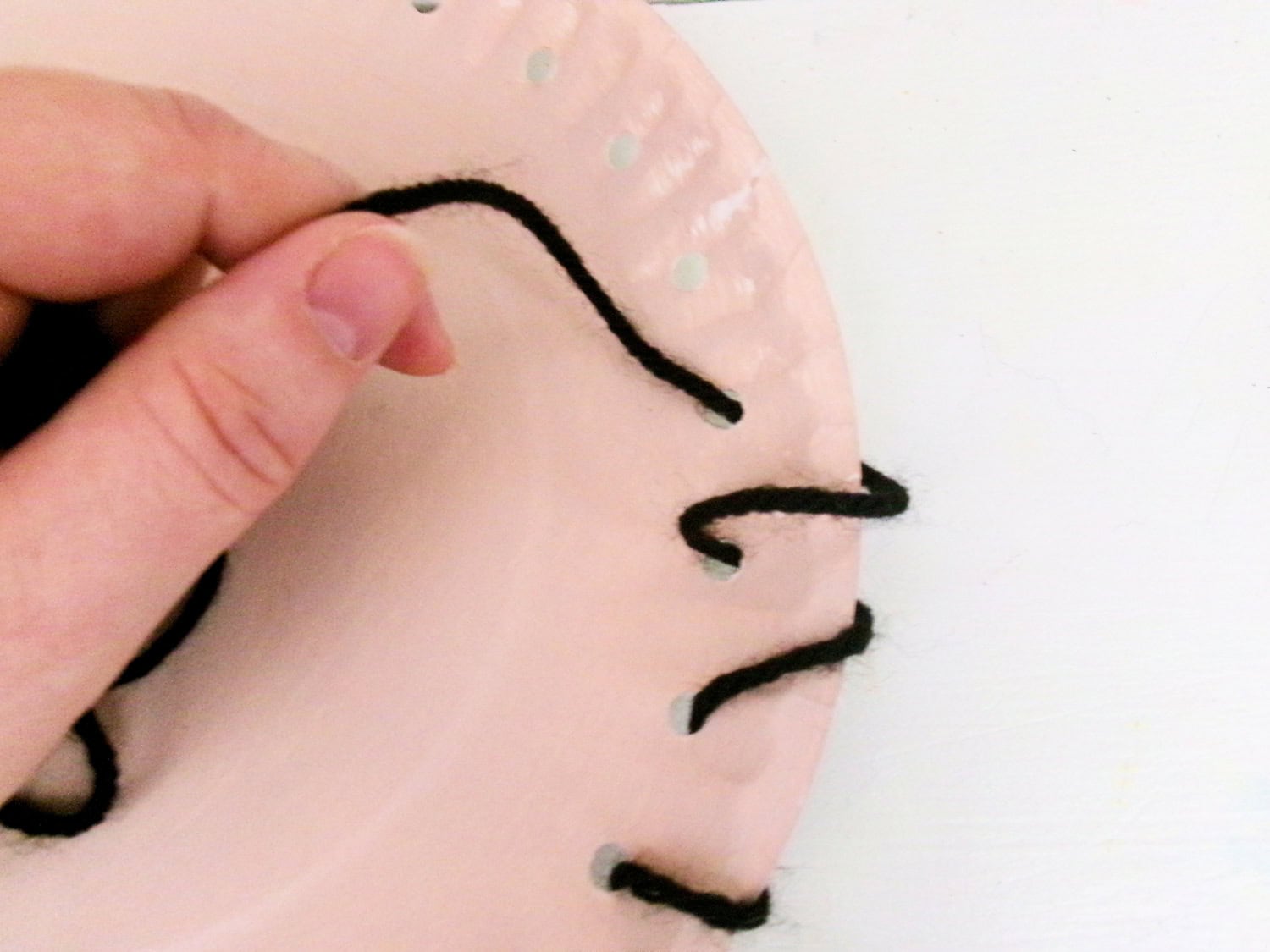 Sticthing the black yarn through the holes of the painted plate for the Paper Plate Scarecrow Craft